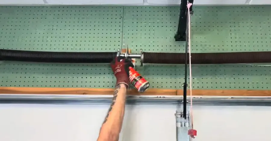 Technician spraying lubricant on a garage door spring during service