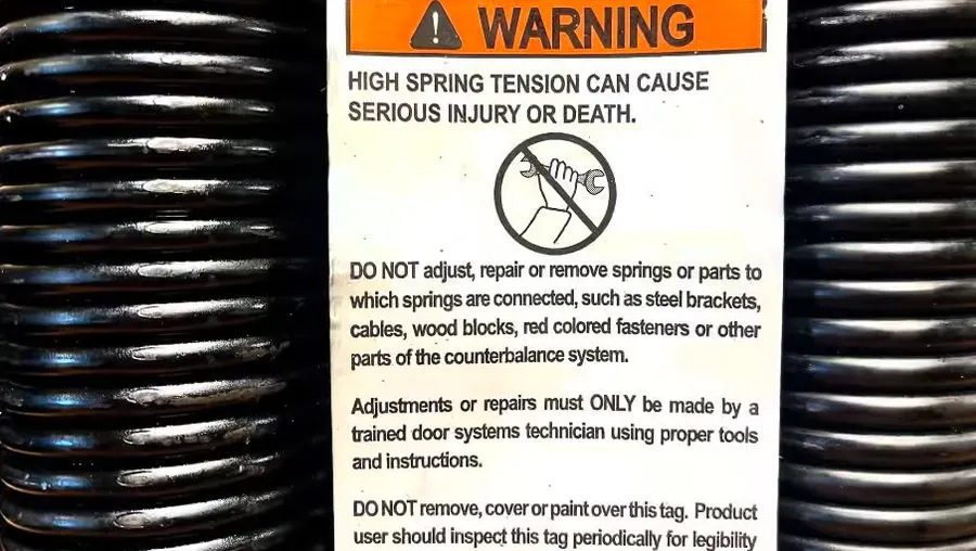 Manufacturer warning label on a garage door torsion spring showing high spring tension danger